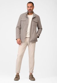 Ljust grå, vattenavvisande jacka med fyra framfickor, dragkedjestängning och en strukturerad yta, i kombination med beige byxor och bruna sneakers.