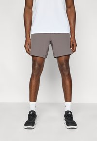 Γκρι αθλητικά σορτς κατασκευασμένα από ελαφρύ ύφασμα, με αεροδυναμική γραμμή, λεία υφή και χωρίς ορατά σχέδια. Μαύρα αθλητικά παπούτσια με λευκές σόλες.