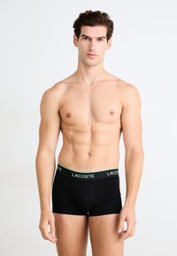 Zwarte boxershorts van zacht materiaal met een groen Lacoste-logo op de elastische tailleband, aansluitend ontwerp en naadloze constructie.