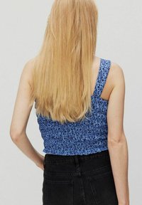 Sininen, hihaton crop-top, jossa on teksturoitu, kerätty muotoilu ja kukkakuosi; yhdistetty korkeavyötäröisiin mustiin farkkuihin.