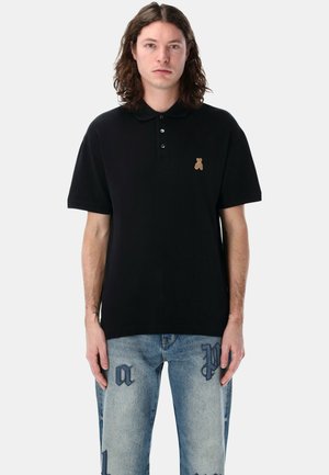 Polo shirt nera in cotone, con un piccolo logo di un orsetto dorato sul lato sinistro del petto, dotata di colletto classico e pattina con tre bottoni.