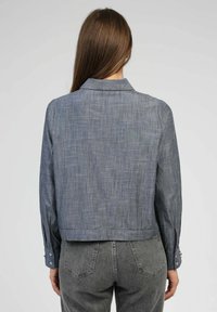 Chemise en chambray gris cropped avec un col, tissu texturé et poignets boutonnés. La vue arrière montre un design épuré sans embellissements.
