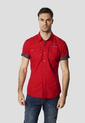 Cămașă roșie cu nasturi și mâneci scurte, având două buzunare frontale, manșete pliabile și un logo discret pe piept.
