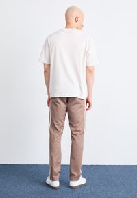 Lichtbeige katoenen t-shirt met een ontspannen pasvorm, gecombineerd met bruine taps toelopende joggingbroeken met witte zijstrepen en witte sneakers.