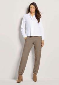 Witte blouse met lange mouwen en een kraag, gecombineerd met bruine jogger-stijl broeken met elastische boorden en zijzakken. Bruine, enkelhoge laarzen met hak.