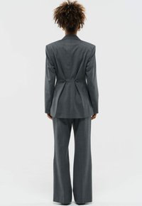 Grijze op maat gemaakte kostuum met een gestructureerde blazer met een cinched achterkant en flared broekspijpen. Gladde stof met een subtiele textuur.