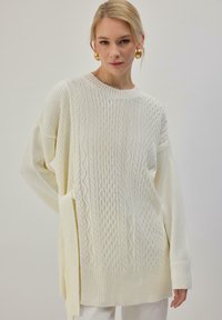 Pull en maille crème avec motifs texturés, manches larges et ourlet côtelé. Coupe décontractée avec fentes latérales pour plus de style.