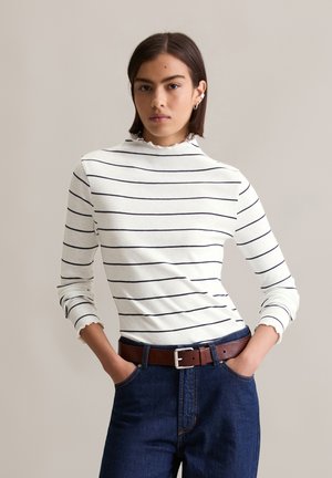 Wit gestreepte lange mouwen top met een hoge halslijn en gerimpelde afwerking, gecombineerd met donkerblauwe denim broek en een leren riem in bruin.
