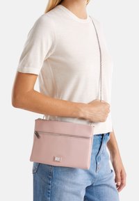 Borsa a tracolla in similpelle rosa con chiusura a zip, superficie testurizzata e tracolla a catena metallica, indossata all'altezza dell'anca su sfondo chiaro.