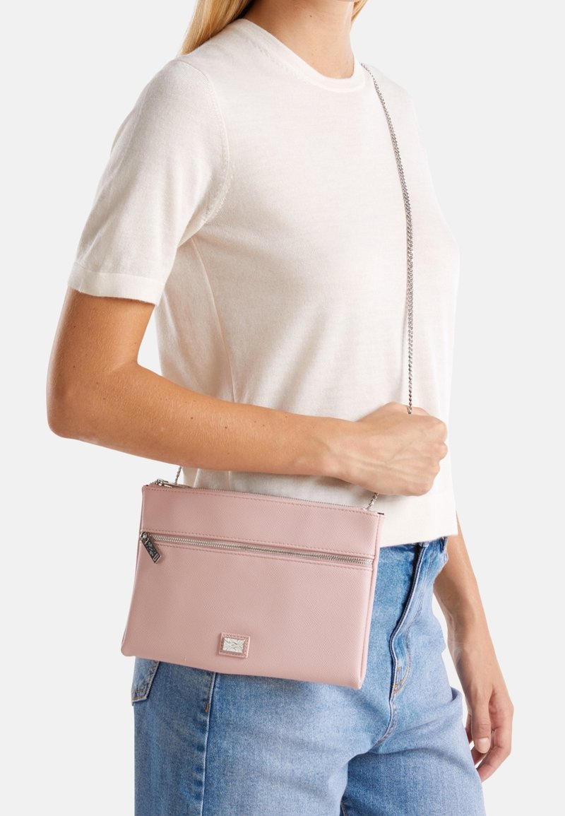 Borsa a tracolla in similpelle rosa con chiusura a zip, superficie testurizzata e tracolla a catena metallica, indossata all'altezza dell'anca su sfondo chiaro.