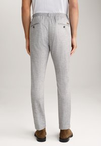 Pantaloni grigi chiari con una finitura testurizzata, vita elastica e due tasche posteriori con chiusura a pulsante. Indossati con scarpe marroni.