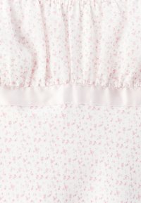 Vit tyg med små rosa blommor och ett horisontellt silkigt ljusrosa band som skiljer mellan de plisserade och släta sektionerna.