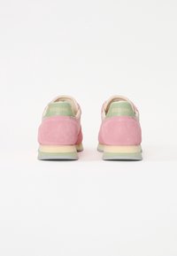 Baskets en daim rose avec des accents vert clair et un intérieur beige. La semelle en caoutchouc est grise avec une légère texture. Logo visible sur le talon.