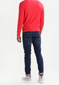 Rode lang mouw shirt in combinatie met donkerblauwe skinny jeans, met een gladde textuur en omgeslagen mouwen. Grijze sneakers met rode en witte accenten.