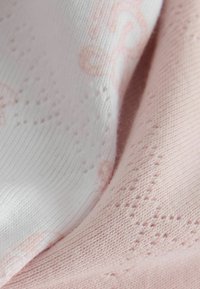 Primo piano di tessuto lavorato a maglia morbido rosa e bianco con delicati motivi a cuore e forme a diamante testurizzate.