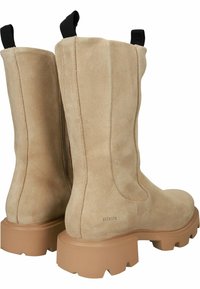 Botines de ante beige con suela de goma gruesa. Presentan tiradores, un acabado suave y acentos negros en la parte superior.