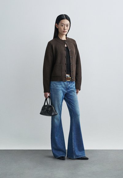 Pruun villa kardigan nööpidega ja kahe esikotiga, kombineeritud laienevate siniste teksadega. Must käekott rõhutab välimust.