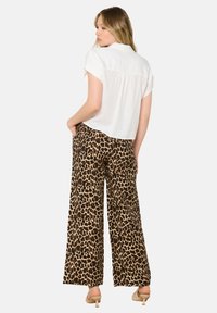 Witte kortekleurige top gecombineerd met brede, leopardenprint broeken. De broeken hebben een zachte, gestructureerde stof met een gedurfde bruine en zwarte patroon.