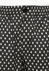 Pantaloni corti neri con un motivo geometrico bianco con forme circolari. Vita elastica con chiusura a bottone e tasche laterali.
