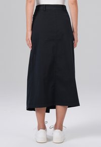 Jupe midi en coton noir avec une coupe droite, dotée d'une taille et de coutures arrière, associée à des baskets blanches pour un contraste.