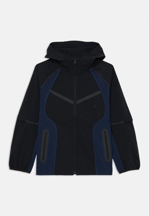 Veste à capuche noire et marine avec fermeture éclair à l'avant, présentant des coutures contrastantes, deux poches zippées et un design sportif et structuré.