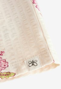 Nærbillede af et lyst lyserødt stofhjørne med et lille hvidt mærke med en sort sommerfuglelogo og lyserødt blomsterbort.