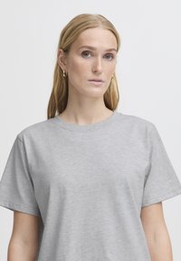 Pilkas medvilnės marškinėliai su trumpomis rankovėmis, apvaliu kaklu ir lygaus paviršiaus. Yra klasikinis dizainas be jokių papildomų raštų ar akcentų.