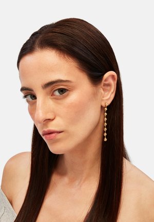 Pendientes colgantes en tono dorado con pequeñas cuentas redondas dispuestas en un diseño graduado, sujetos a ganchos para orejas perforadas.