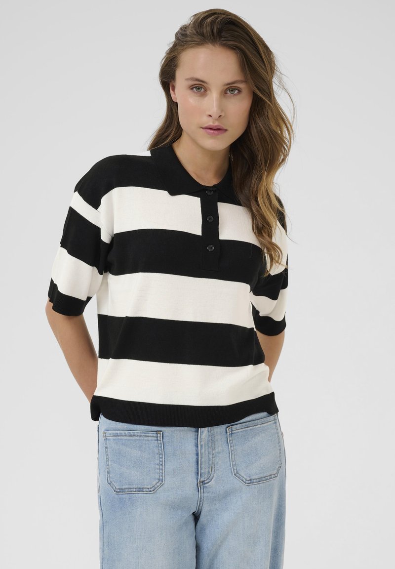 Zwart-wit gestreepte polo met korte mouwen, knoopsplit en ribgebreide kraag. Draagt met lichtblauwe jeans, voorzien van achterzakken.
