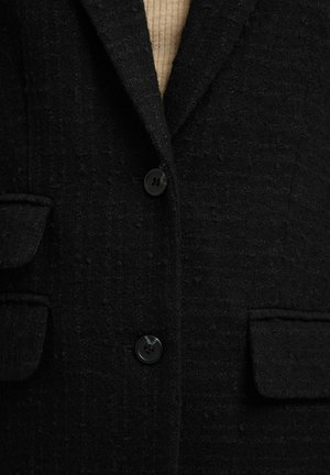 Schwarzer Blazer mit strukturierter Oberfläche, gekerbtem Revers, zwei Fronttaschen und Ein-Knopf-Verschluss. Verfügt über dezente Stoffdetails und glatte Knöpfe.