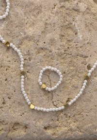 Set di gioielli in perle composto da una collana e un anello, con perle bianche lisce e accenti a forma di cuore in oro.