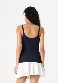 Top de tirantes ajustables en color azul marino, combinado con una falda blanca con dobladillo rizado; diseño ajustado, textura suave. Vista trasera.
