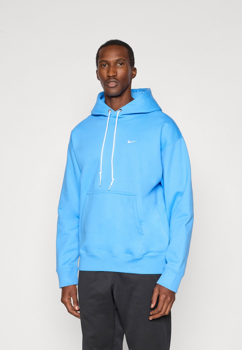 Kapuzenpullover aus leuchtend blauem Baumwollstoff, mit einer Fronttasche, weißen Kordeln und einem kleinen weißen Logo auf der Brust.