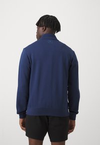 Marineblå sweatshirt med høj krave, ribstrikkede manchetter og kant. Har et diskret logo præget på den bageste halskant. Fremstillet af blødt stof.