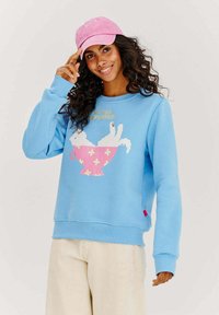 Svetlomodrý sweatshirt s grafickým motifom ružového šálky s bielou mačkou. Dlhé rukávy, rebrované manžety a lem. V kombinácii s ružovou šiltovkou.