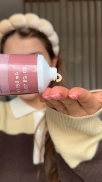 Tubo rosa e bianco che eroga una crema su una mano, evidenziando la texture liscia e il design arrotondato. Il tubo mostra l'etichetta da 150 mL.