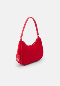 Rød nylon skuldertaske med en buet form, lynlåslukning og et logo-mærke med "SM." Remmen er slank og justerbar.