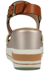 Braune Leder-Sandaletten mit Knöchelriemen, goldenem Schnallenverschluss, metallisch bronzefarbenem Plateau, weiß-beigem Absatz und geflochtenem Detail im oberen Bereich.