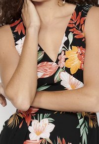 Vestido floral con fondo negro; cuenta con un escote en V profundo, patrones florales coloridos en naranja, rosa y verde; diseño sin mangas.
