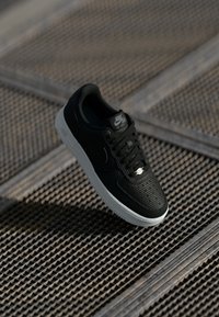Crne Nike Air Force 1 tenisice s teksturiranim gornjim dijelom, ravnim crnim vezicama i bijelim međuslojem. Sadrže logotip na jeziku i bočnoj strani.