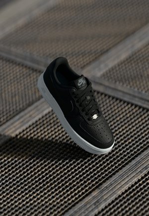 Mustad must Nike Air Force 1 sneaker, millelõikega ülemine osa, lame mustad paelad ja valge vaheosa. Omab logo keelel ja küljel.