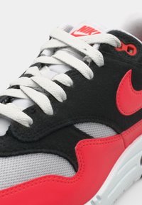 Pantofi Nike cu un superior din suede negru, accente coral strălucitor, plasă albă și șireturi plate albe. Branding vizibil pe limbă.