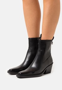Černé kožené kotníkové boty s špičatou špičkou, bočním zipem a blokovým podpatkem. Hladká textura s jemnými detaily prošívání.