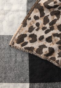 Coperta a quadri caratterizzata da un mix di motivi grigi, neri e bianchi, con un accento in stampa leopardata beige e marrone, e bordi frangiati.