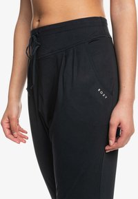 Mustat verryttelyhousut, joissa on naru vyötäröllä, sivutaskut ja Roxy-logo edessä. Sujuva pinta ja rento malli.