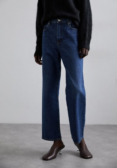 Blue denim jeans with a loose fit and straight leg, featuring a regular waistband and subtle front stitching details, paired with brown heeled mules.