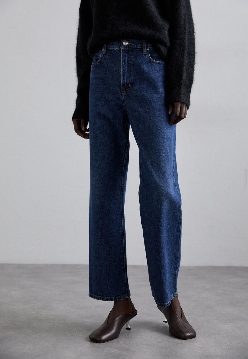 Blauwe denim jeans met een losse pasvorm en rechte pijpen, voorzien van een reguliere tailleband en subtiele stiksels aan de voorkant, gecombineerd met bruine hakken mules.