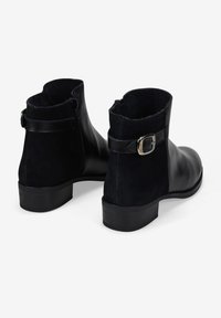 Botas de tobillo negras hechas de ante y cuero, con cremalleras laterales, correa con hebilla de plata y tacón bajo.