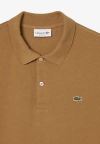 Polo marrón de algodón, con un cuello clásico, tapeta de tres botones y un logo de cocodrilo bordado en el pecho.