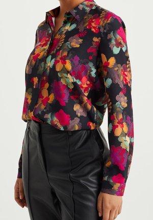 Blusa floral con fondo negro, con flores vibrantes en rojo, rosa y verde azulado. Mangas largas, diseño abotonado, tela suave.
